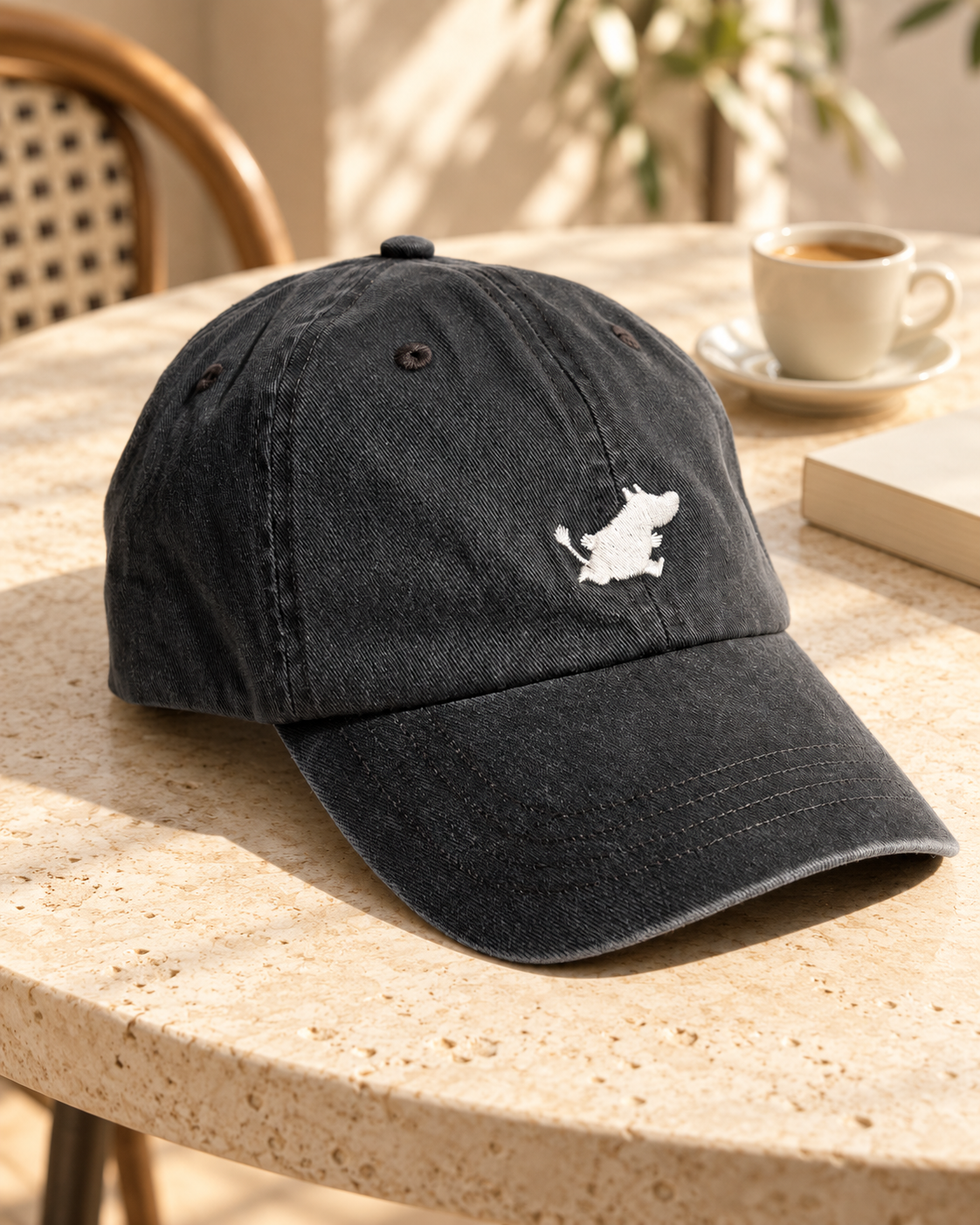 Casquette Moomin Classics en denim gris foncé avec motif blanc, posée sur une table de café