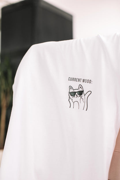 Gros plan du motif chat à lunettes et de l'inscription Current Mood sur le t-shirt blanc